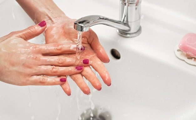 Mujer joven lavándose las manos bajo el grifo de agua. Detalle de líquido sobre piel. concepto de higiene personal