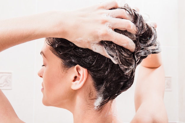 Mujer joven lavarse el cabello con champú en la ducha