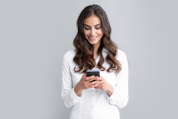 mujer joven, lectura, mensaje, en, teléfono móvil, y, sonriente, feliz, mujer de negocios, con, smartphone, posición, en, fondo gris