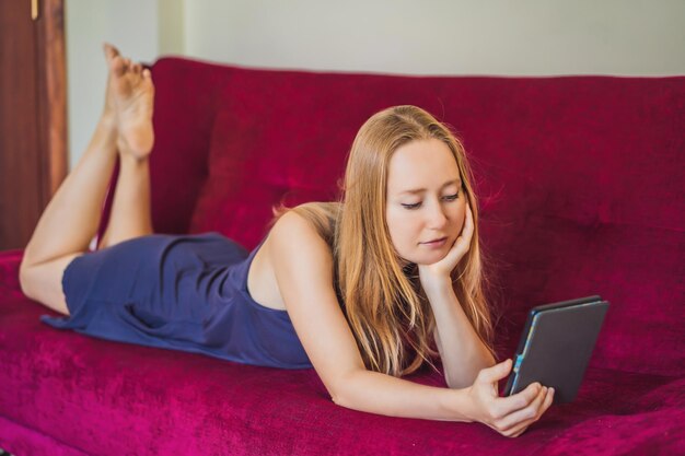 Mujer joven lee ebook en casa en el sofá