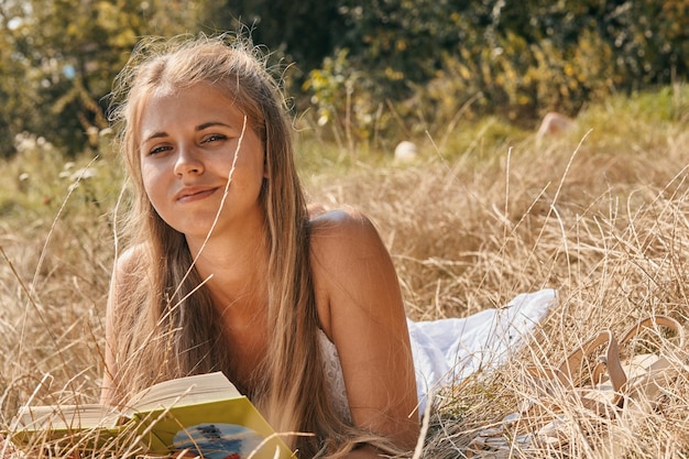 mujer joven, leer un libro, acostado, en, pasto o césped