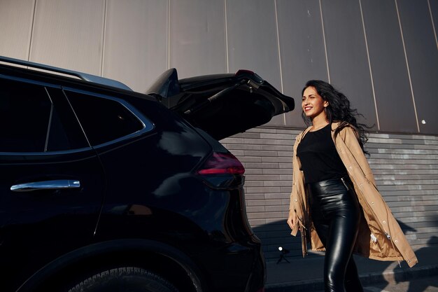 Mujer joven en leggins negros sale de su coche moderno