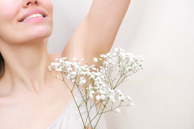 Mujer joven levantando sus manos y mostrando axilas con gypsophila en su mano, axilas piel suave y transparente