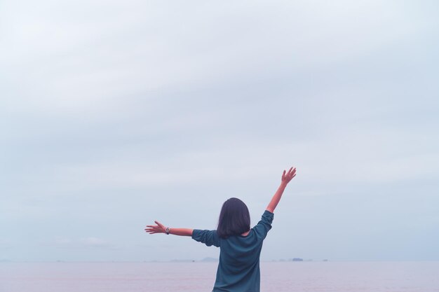 Mujer joven levantar la mano hacia el cielo sentirse relajado y libre con fondo de playa de verano