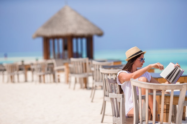 Mujer joven leyendo en el café de la playa al aire libre