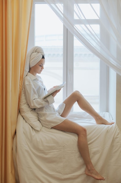 Mujer joven leyendo un libro al lado de la ventana después de levantarse por la mañana Concepto de estilo de vida matutino
