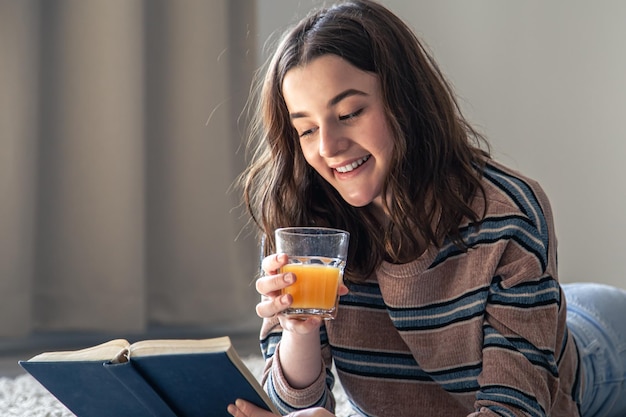 Foto una mujer joven está leyendo un libro y bebiendo jugo de naranja.