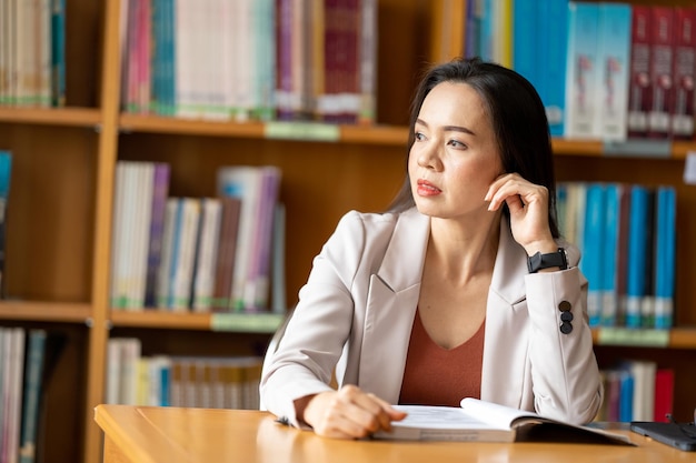 Mujer joven leyendo un libro en la biblioteca de la universidad