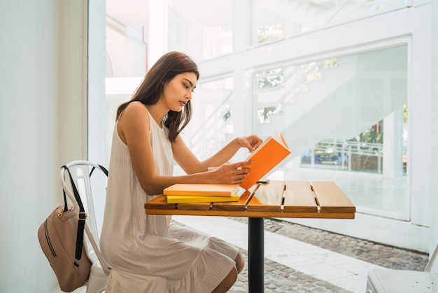 Mujer joven leyendo un libro en la cafetería.