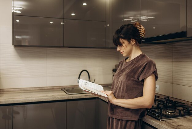 Mujer joven leyendo un libro de cocina en la cocina buscando una receta