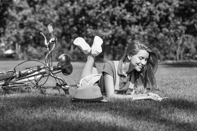 Mujer joven leyendo un libro después de andar en bicicleta en el parque local.