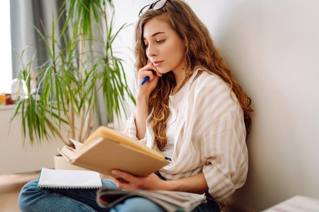 Mujer joven leyendo un libro escribiendo notas haciendo tareas en casa Concepto de descanso relajación