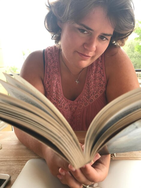 Foto mujer joven leyendo un libro mientras está sentada en la mesa