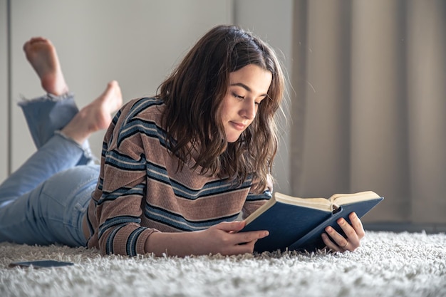 Foto una mujer joven está leyendo un libro sentada en el suelo de su habitación.