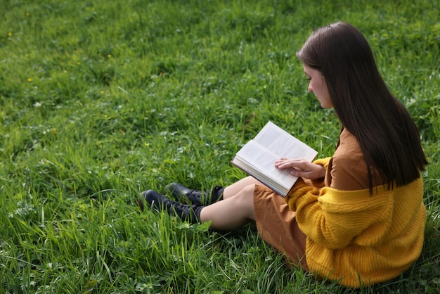 Mujer joven leyendo un libro sobre la hierba verde