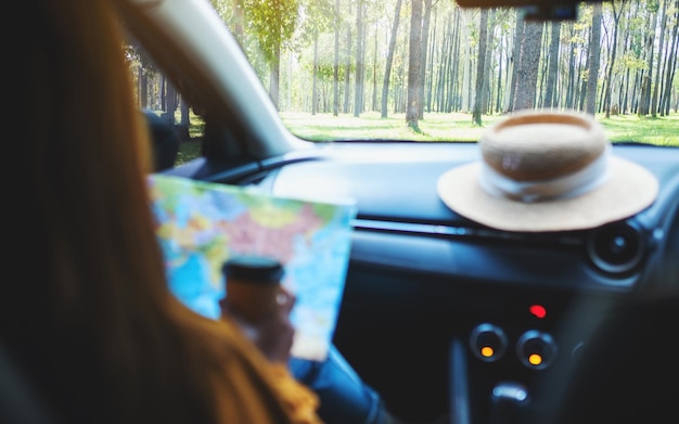 Una mujer joven leyendo un mapa de dirección y bebiendo café mientras está en el auto