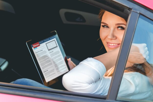 Foto mujer joven leyendo noticias con tableta en manos sentado en el coche