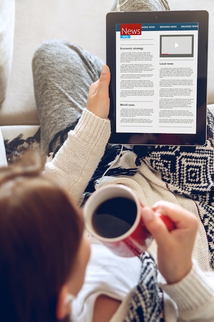 Mujer joven leyendo noticias con tableta mientras está sentado en el sofá en casa