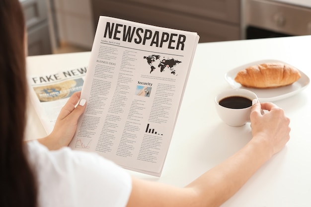 Mujer joven leyendo el periódico mientras bebe café en la cocina