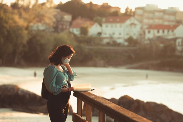 Mujer joven leyendo en la playa durante una súper puesta de sol mientras usa una máscara relajarse