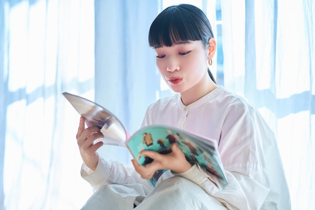 Mujer joven leyendo una revista junto a la ventana