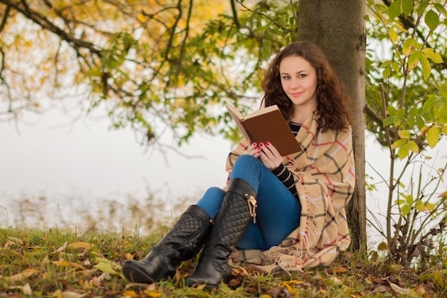 Mujer joven con libro en el parque en otoño