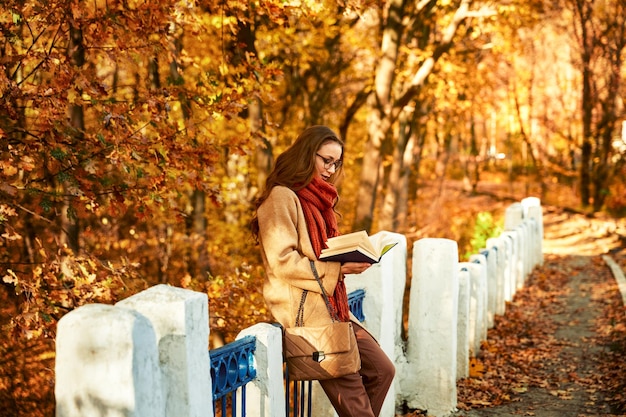 Mujer joven con libro en el parque de otoño