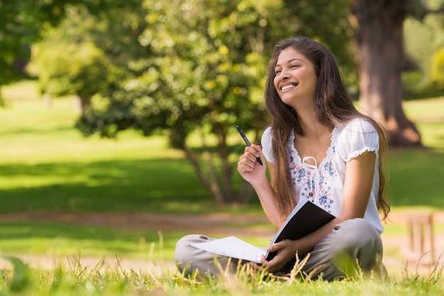 Mujer joven con libro y pluma sentado en el parque