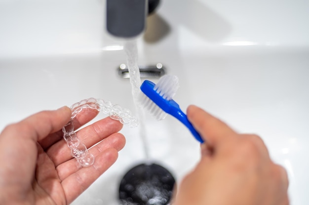 Mujer joven limpiando un alineador dental invisible con un cepillo