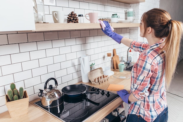 Mujer joven limpiando los muebles de la cocina.