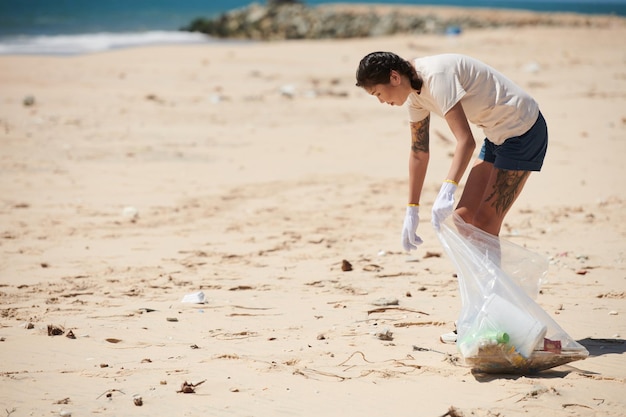 Mujer joven limpiando la playa del mar recogiendo basura en una bolsa de plástico