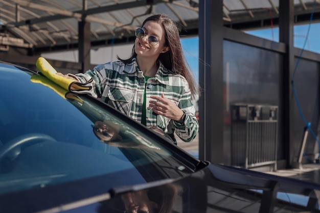 Una mujer joven limpiando y puliendo su auto con un paño amarillo de microfibra Concepto de cuidado del auto