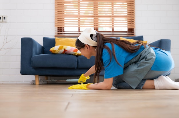 Mujer joven limpiando el suelo con un trapeador debajo del sofá en la sala de estar