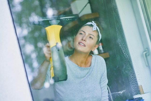 Mujer joven limpiando ventana en la cocina