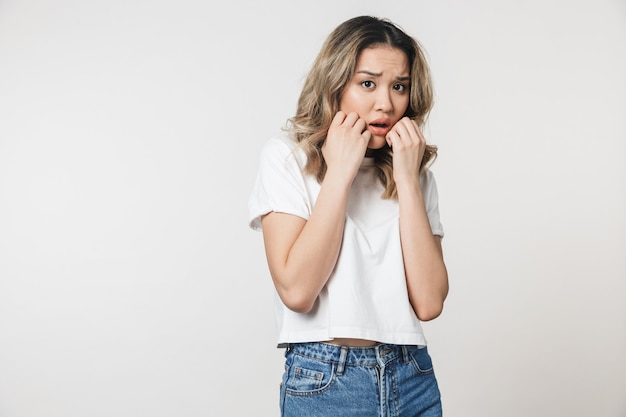 Una mujer joven linda emocional triste asustada posando aislada sobre la pared de la pared blanca