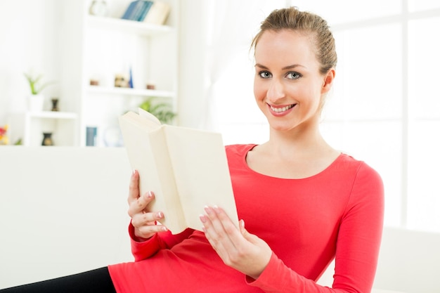 Mujer joven linda feliz en el libro de lectura casero