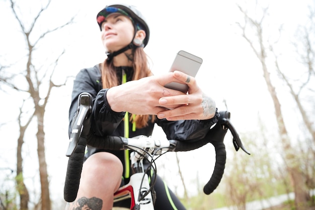 Mujer joven linda pensativa en bicicleta con teléfono móvil en el parque