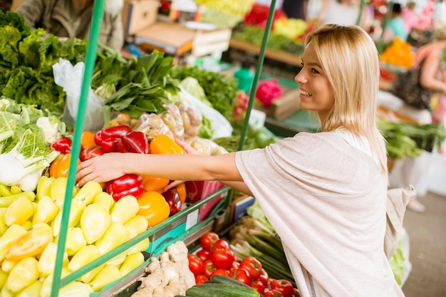 Mujer joven linda que compra verduras en el mercado