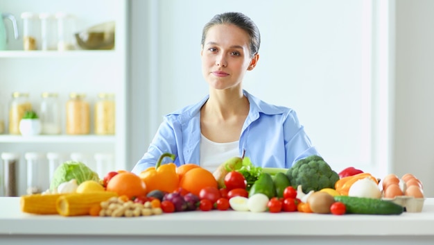 Mujer joven y linda sentada en la mesa llena de frutas y verduras en el interior de madera