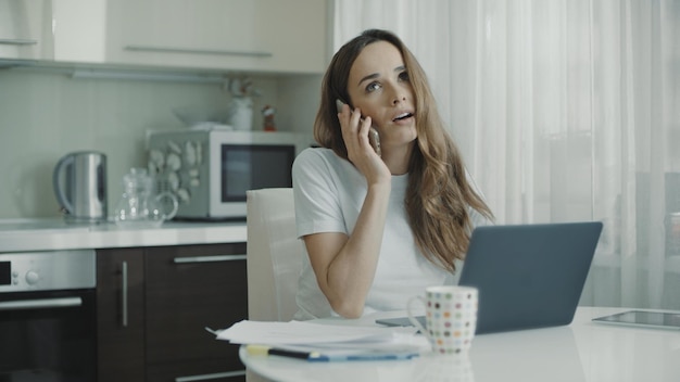 Foto mujer joven, llamada, teléfono, en casa, cocina, mujer de negocios, hablar, teléfono móvil