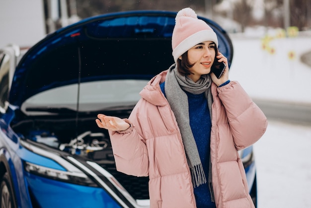 Mujer joven llamando por teléfono después de que su auto se averió en la temporada de invierno