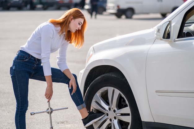 Mujer joven con llave esperando ayuda para cambiar la rueda