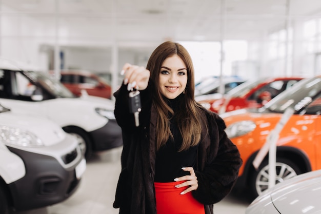 Foto una mujer joven con las llaves de su auto nuevo en una tienda de autos