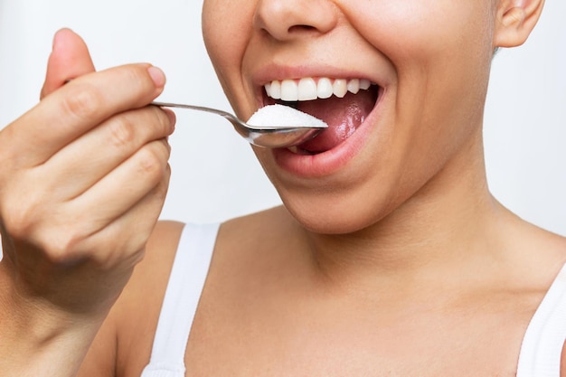 Mujer joven llevándose una cucharada de azúcar blanca a la boca. Dependencia, daño y peligro para la salud.
