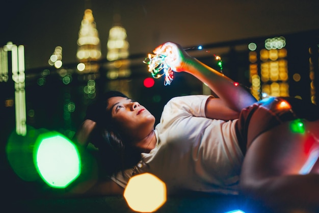 Foto mujer joven con luces iluminadas acostada en la habitación