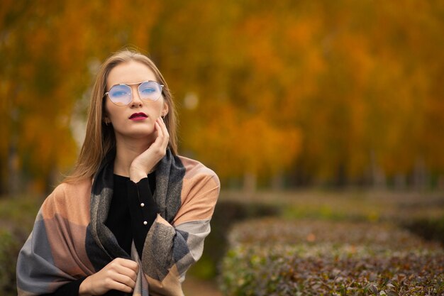 Foto mujer joven de lujo con bufanda de moda y gafas de sol posando en el parque de otoño. espacio para texto