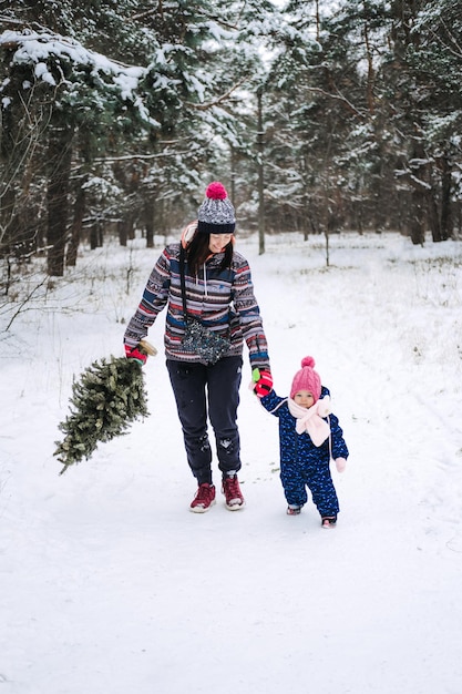 Mujer joven madre soltera y una niña pequeña lleva el árbol de Navidad en el Winter Park preparándose para