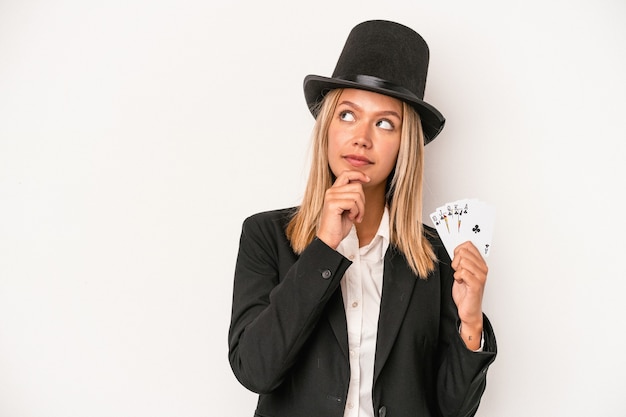 Mujer joven mago caucásico con tarjeta mágica aislada sobre fondo blanco mirando hacia los lados con expresión dudosa y escéptica.