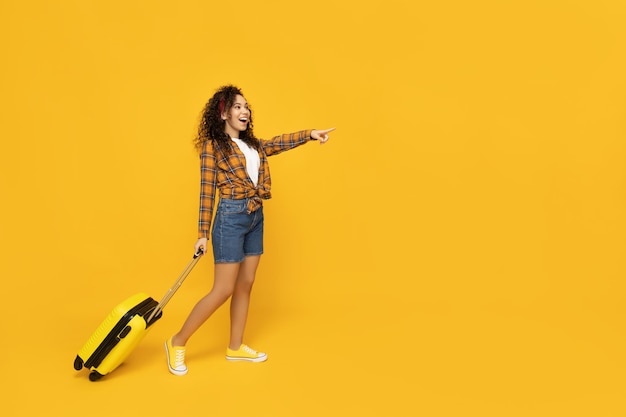 Mujer joven con maleta sobre fondo amarillo