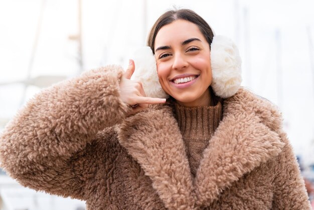 Foto mujer joven con manguitos de invierno al aire libre haciendo gestos de teléfono llámame firmar